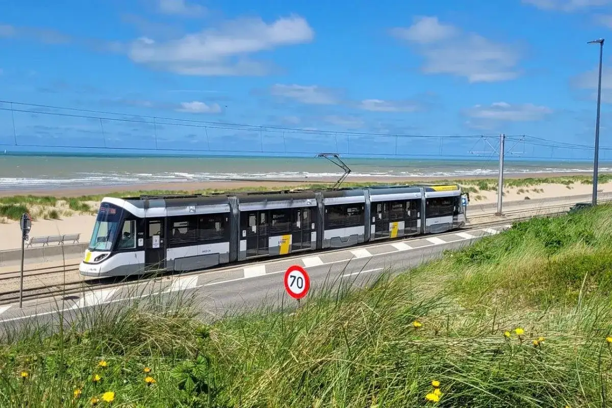 Nowoczesny tramwaj jedzie wzdłuż plaży, potwierdzając, że Belgia ma dostęp do morza.