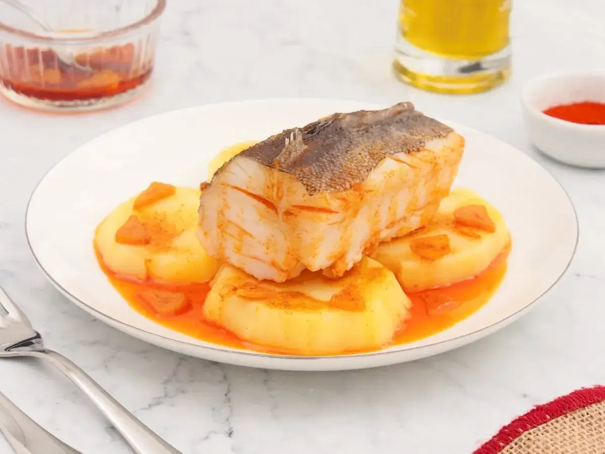 Un delicioso bacalao a la gallega, con patatas y piment&oacute;n, servido en un plato blanco.