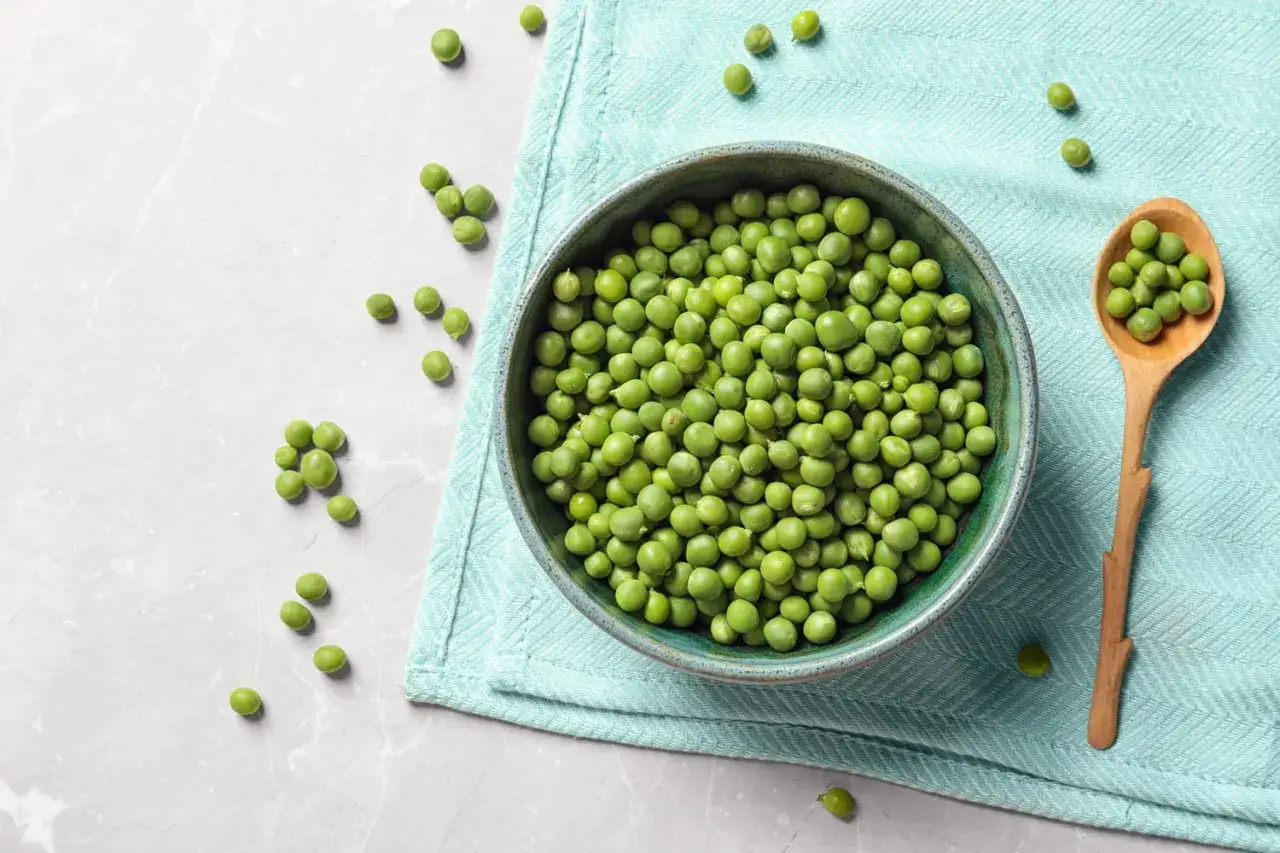 Bol rempli de petits pois frais prêts pour la cuisson. Une cuillère en bois déborde de ces joyaux verts.