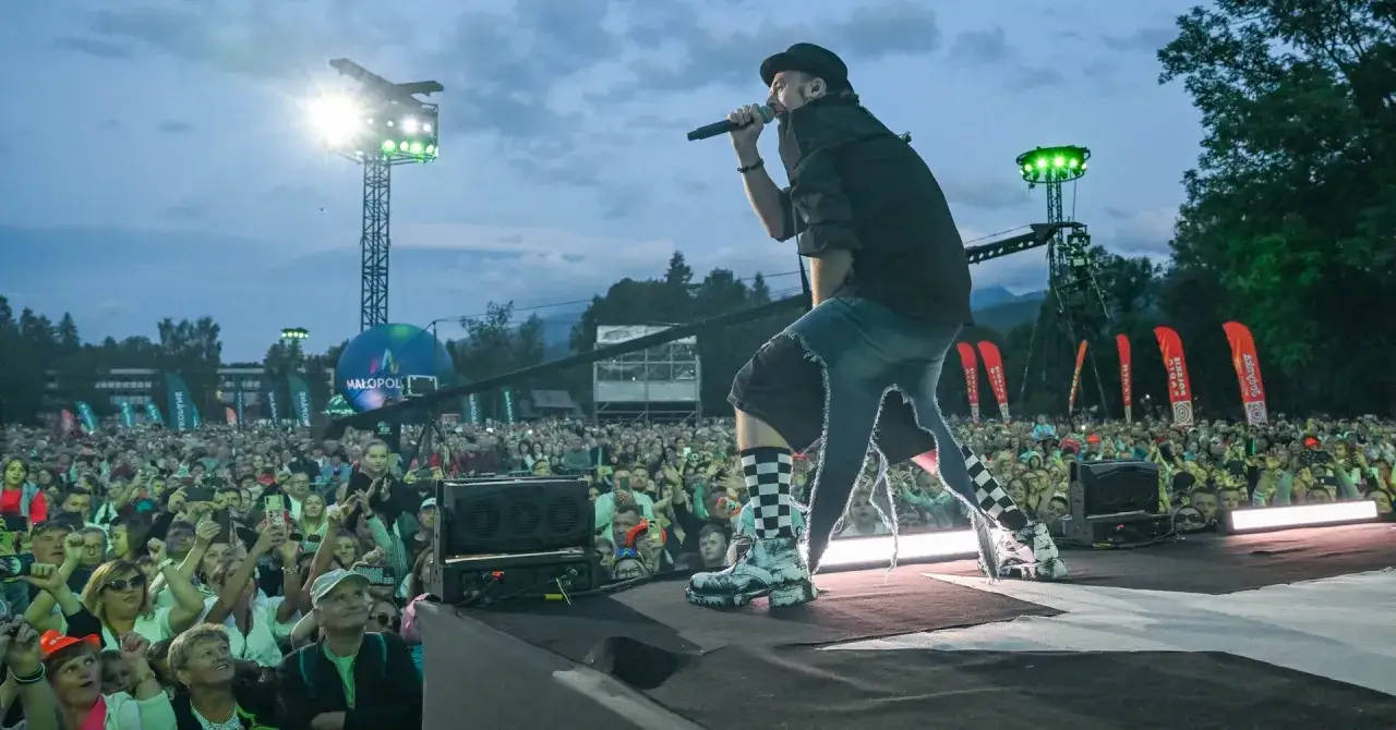Artysta w czapce i z mikrofonem na scenie, tłum ludzi na koncercie w Zakopanem.