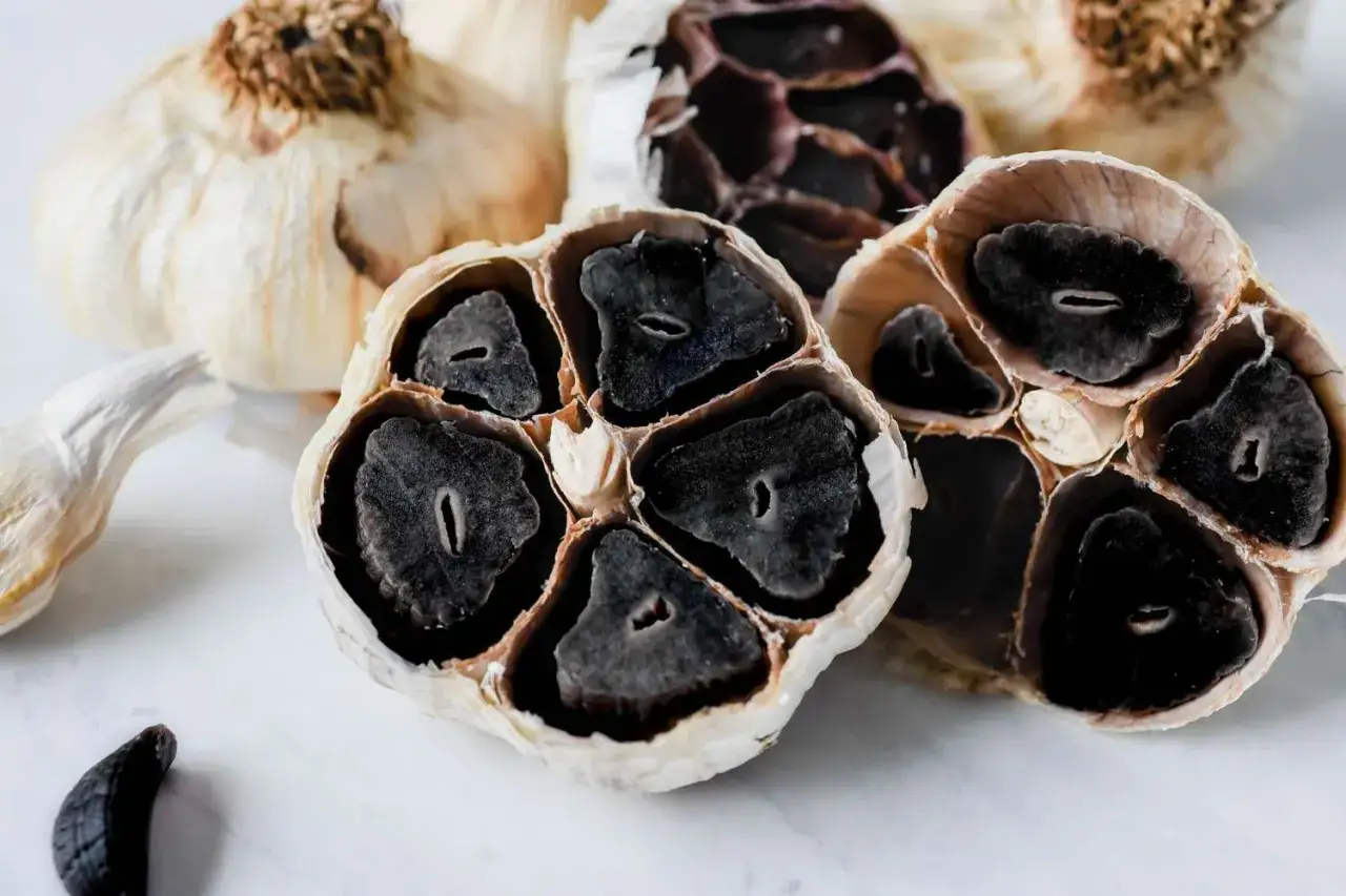 Schnittansicht von fermentiertem Knoblauch mit tiefschwarzen Zehen. Ein einzelner Zeh liegt daneben.