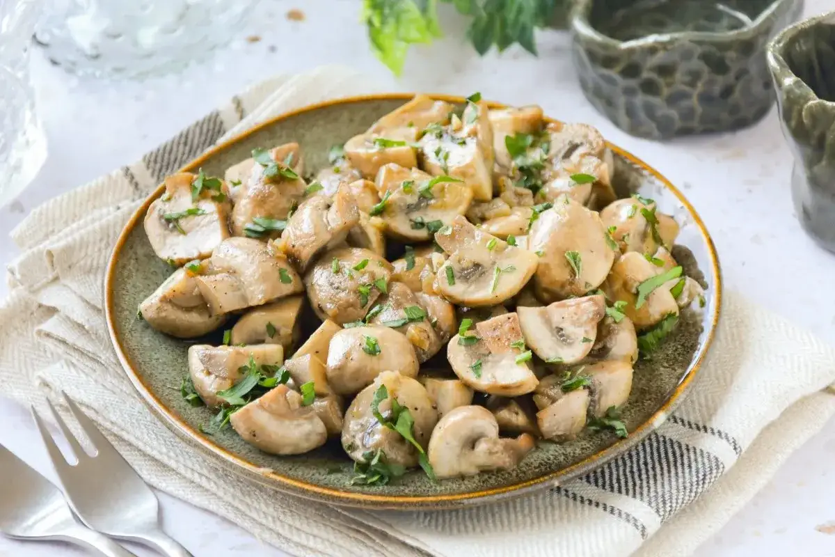 Champiñones salteados con cebolla, picados y espolvoreados con perejil fresco, servidos en un plato rústico.