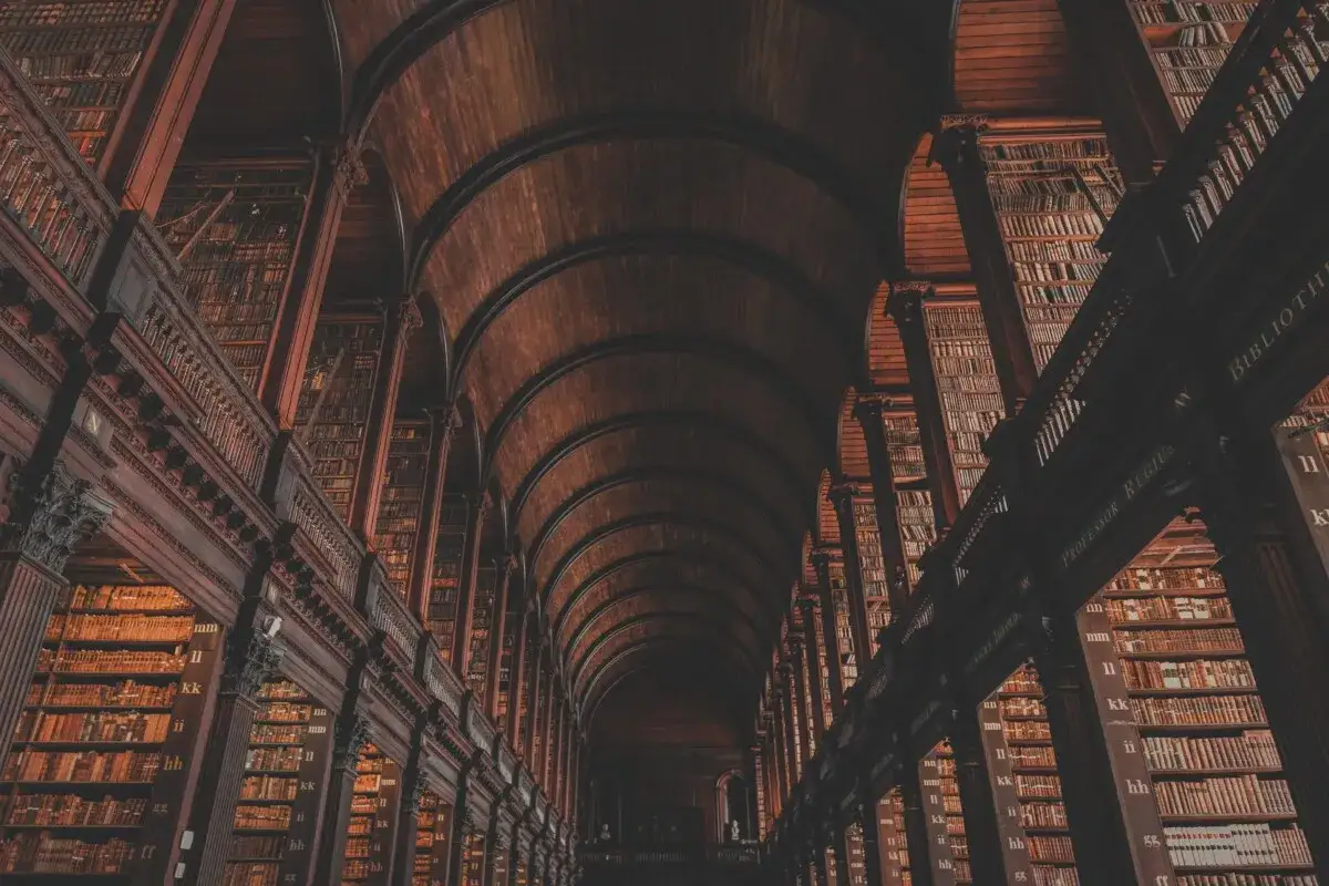Pasillos de biblioteca antigua, estanterías de madera oscura repletas de libros. Un ambiente que evoca el