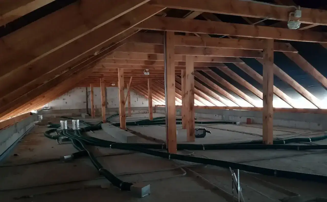 Na strychu widać instalację wentylacyjną z zielonymi rurami, przygotowaną pod montaż rekuperatora. Drewniana konstrukcja dachu jest widoczna.