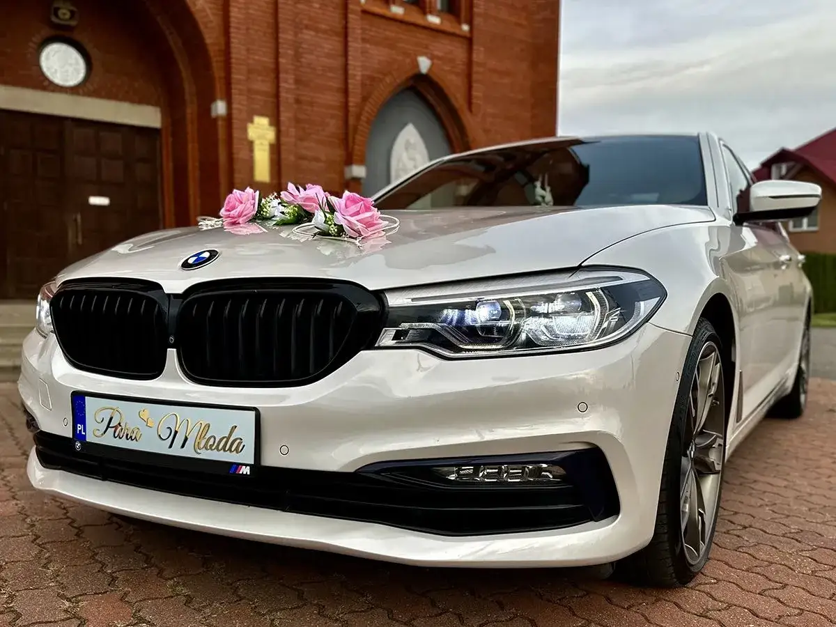 Eleganckie BMW z różowymi kwiatami na masce, gotowe na ślub. Zastanawiasz się, ile kosztuje wynajem samochodu do ślubu?