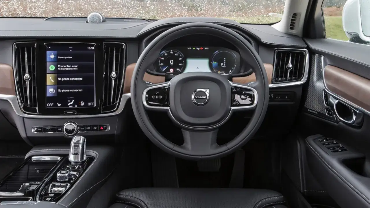 Wnętrze Volvo V90 T8 z ekranem dotykowym, cyfrowymi zegarami i drewnianymi wstawkami.