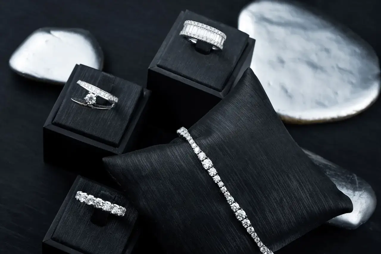 Gioielli scintillanti, anelli e bracciali con diamanti, esposti su supporti neri.