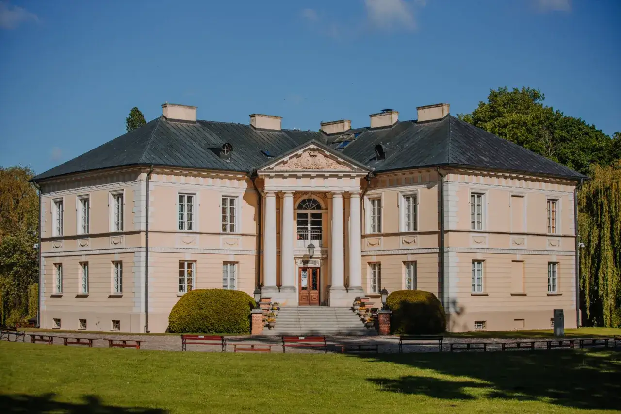 Pałac w Dobrzycy Wielkopolskiej, otoczony zielenią, z klasycystyczną fasadą i kolumnowym portykiem.