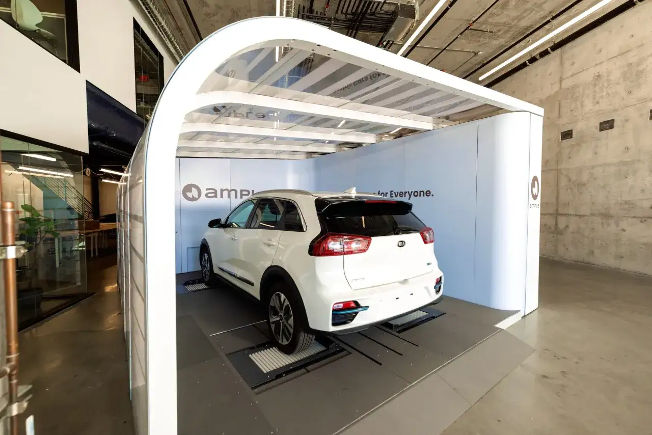 Stazione di **battery swap** per auto elettriche. Una Kia bianca è posizionata su una piattaforma per la sostituzione rapida della batteria.