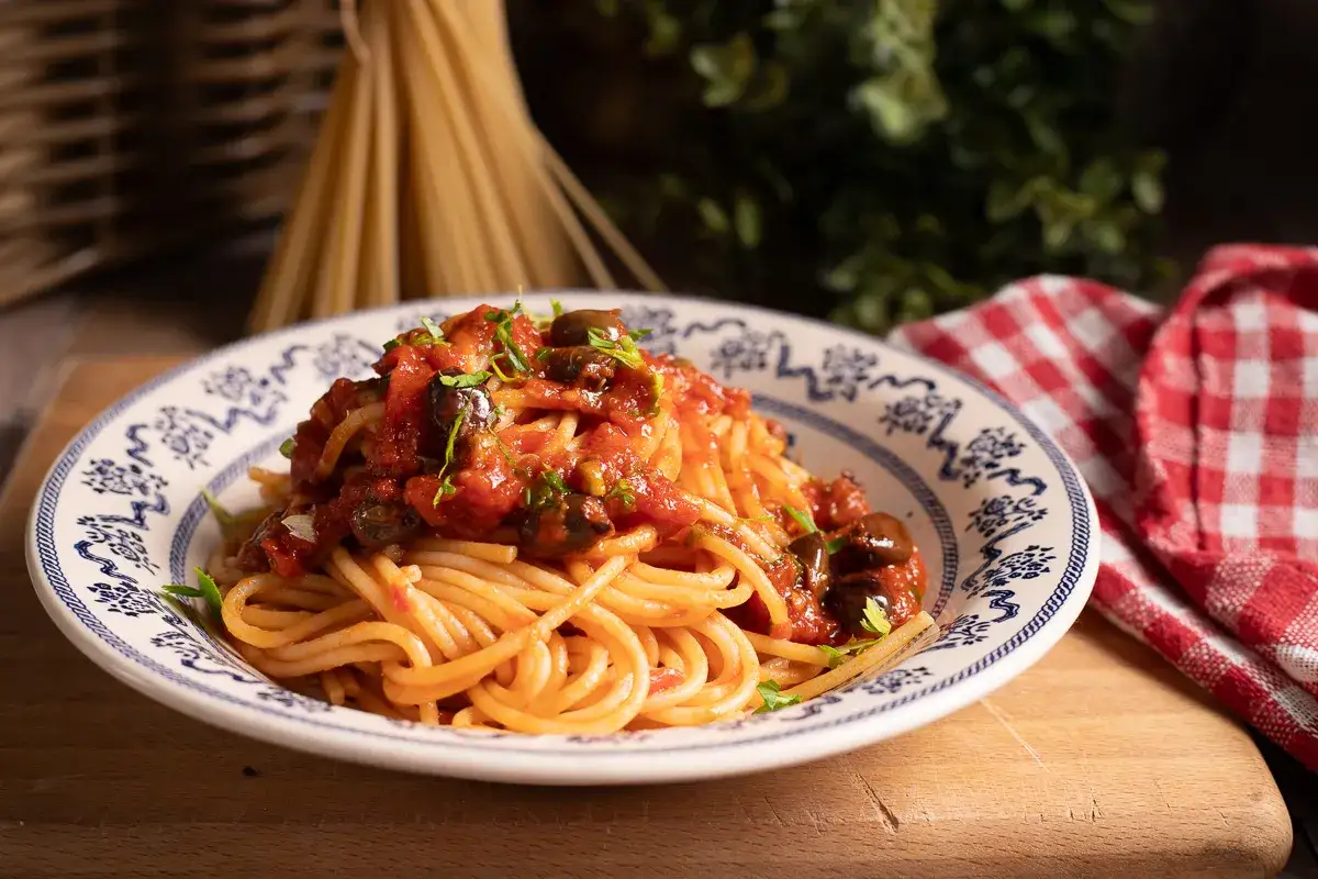 Un piatto di spaghetti alla puttanesca, conditi con pomodoro, olive e capperi, guarniti con prezzemolo fresco.