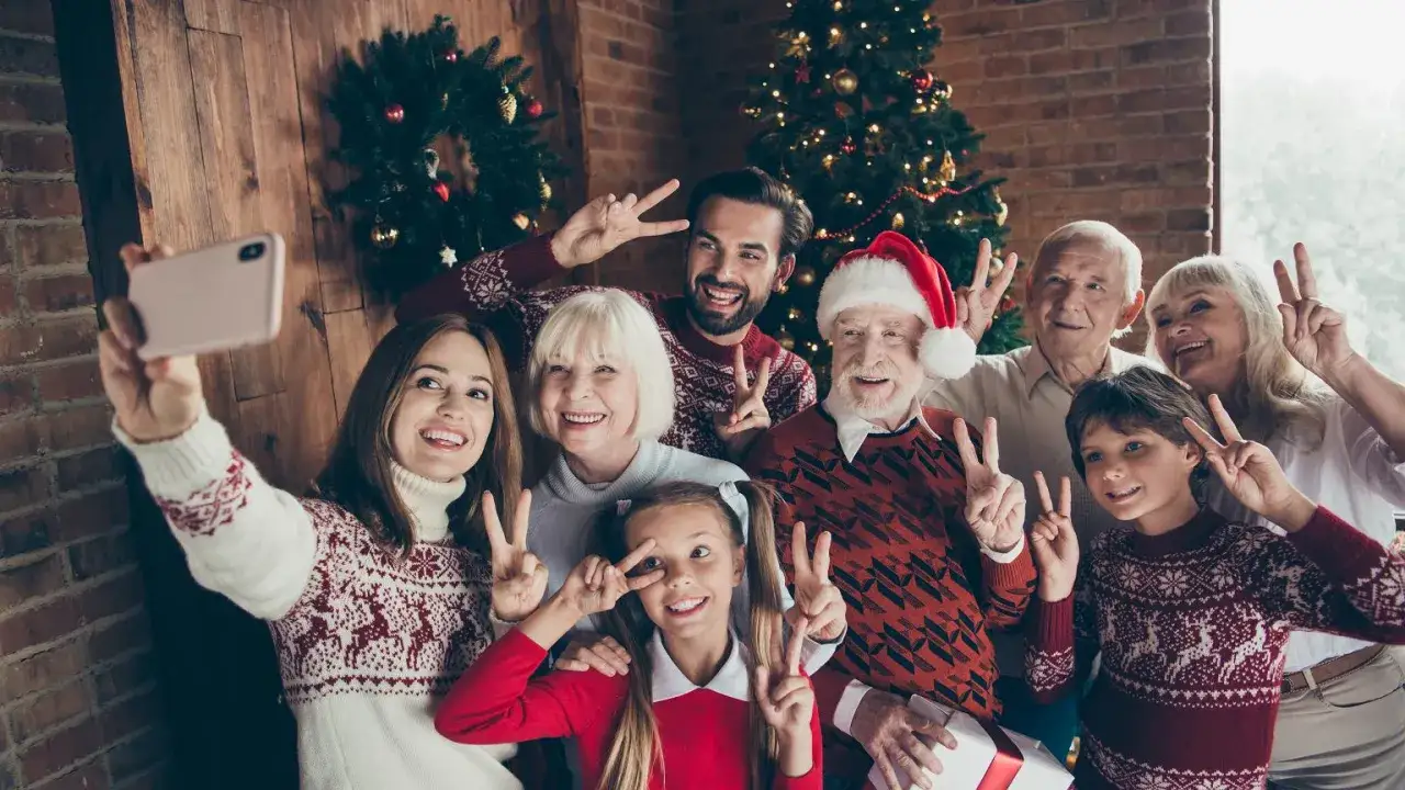 Rodzina w świątecznych swetrach robi sobie selfie przy choince. Wszyscy pozują z uśmiechem, pokazując znak pokoju. To idealny strój na święta!