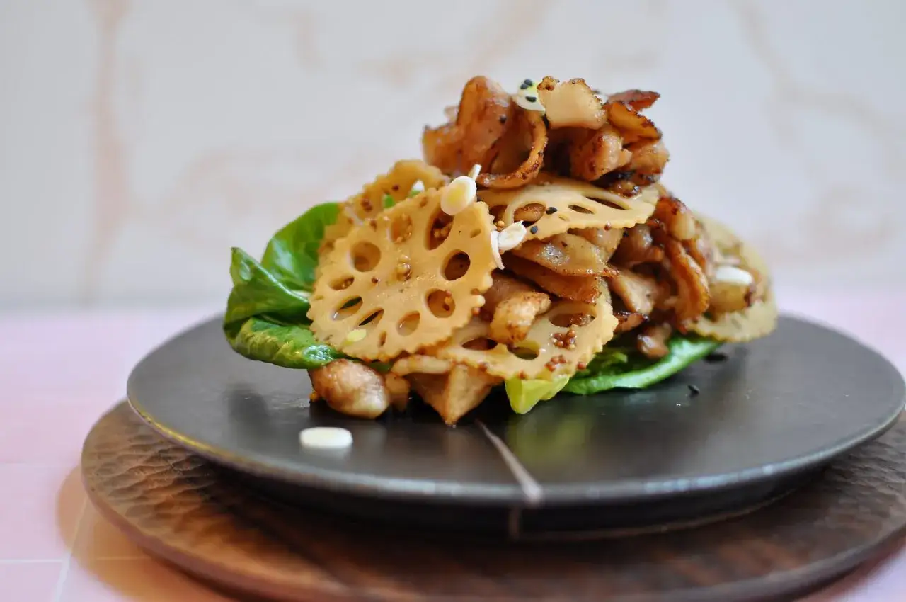 A delicious stack of crispy pickled lotus root slices, seasoned with mustard seeds and black sesame, served on a bed of lettuce.