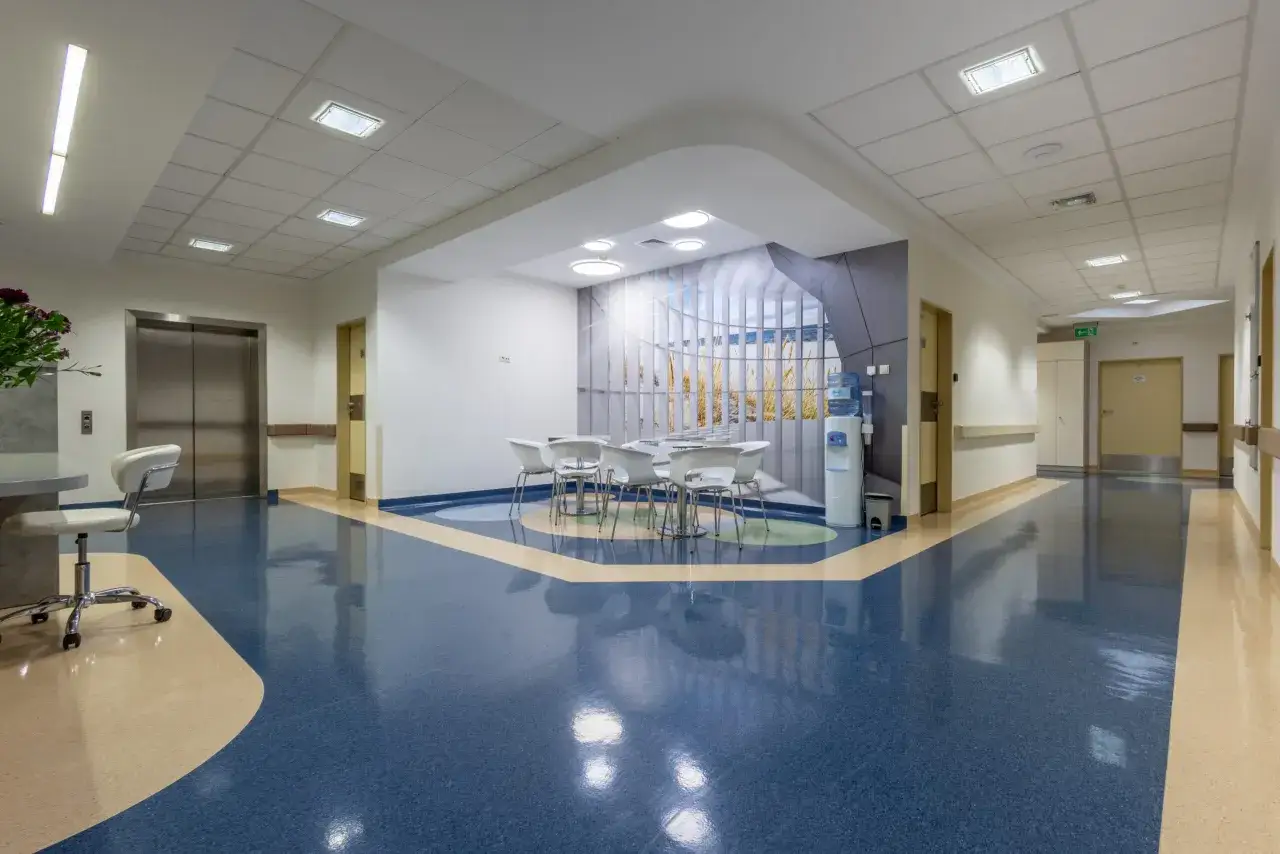 Nowoczesny hol kliniki z windą, poczekalnią i muralem z widokiem na plażę.