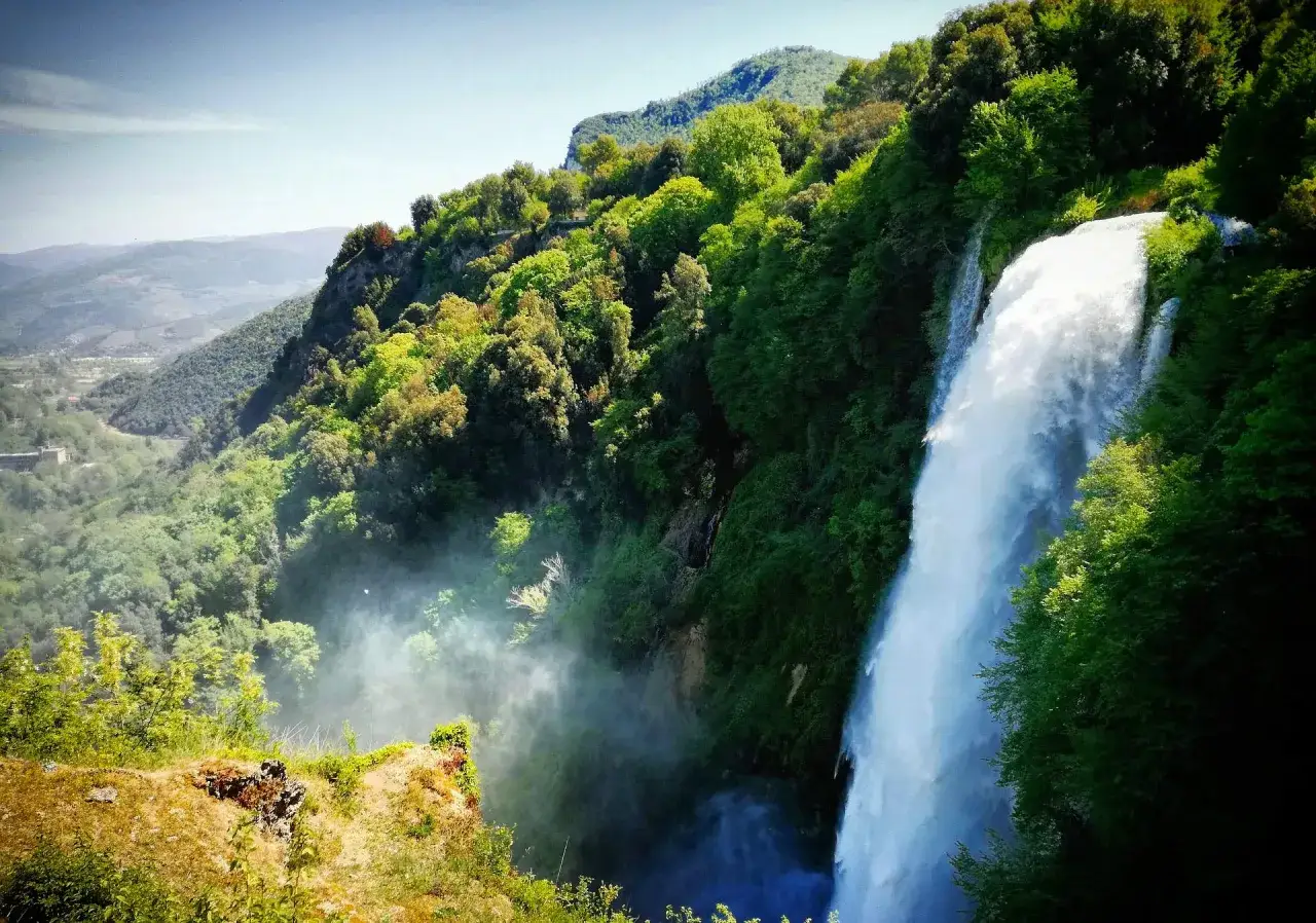 Cascata imponente tra i verdi monti dell'Umbria, con la nebbia che sale dal fondovalle.