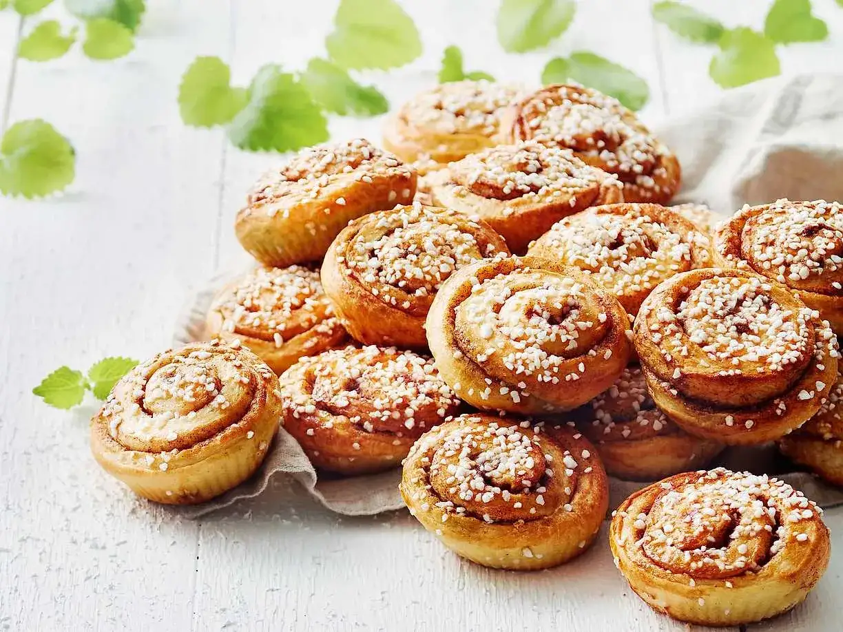 En hög med gyllene kanelbullar, toppade med pärlsocker. Perfekt för ett mysigt fika eller när du vill baka ett gott kanelbullar recept.