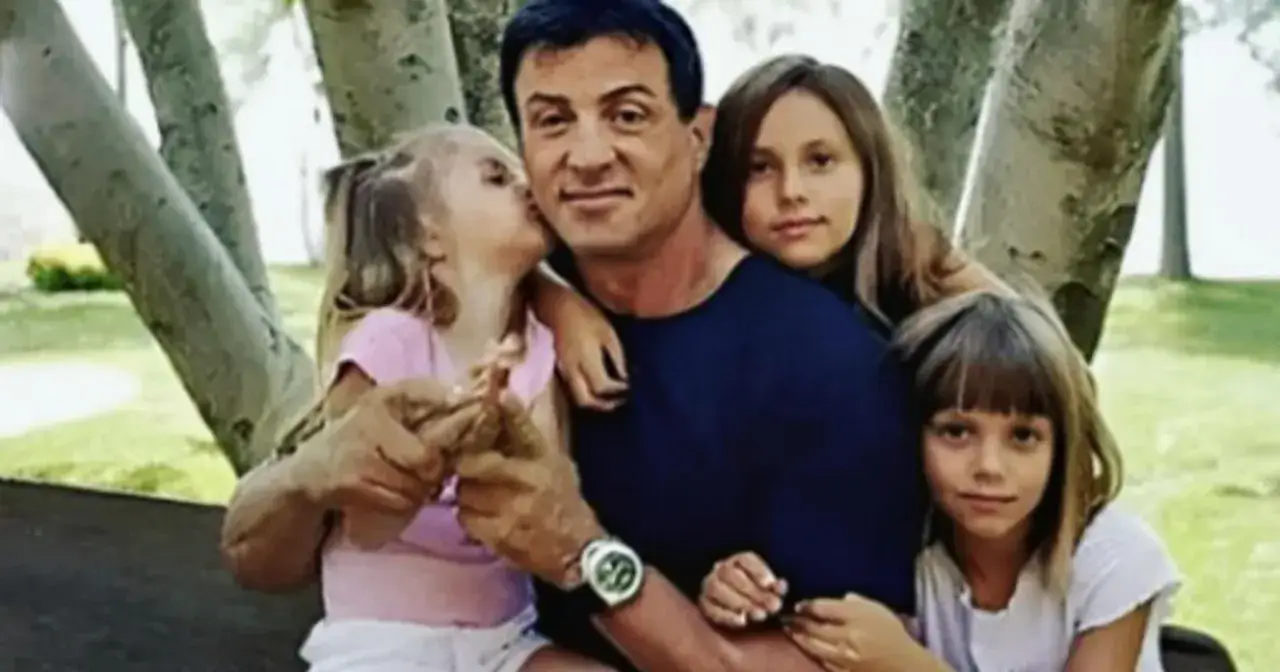 Sylvester Stallone z córkami. Jedna całuje go w policzek, druga opiera głowę na ramieniu.