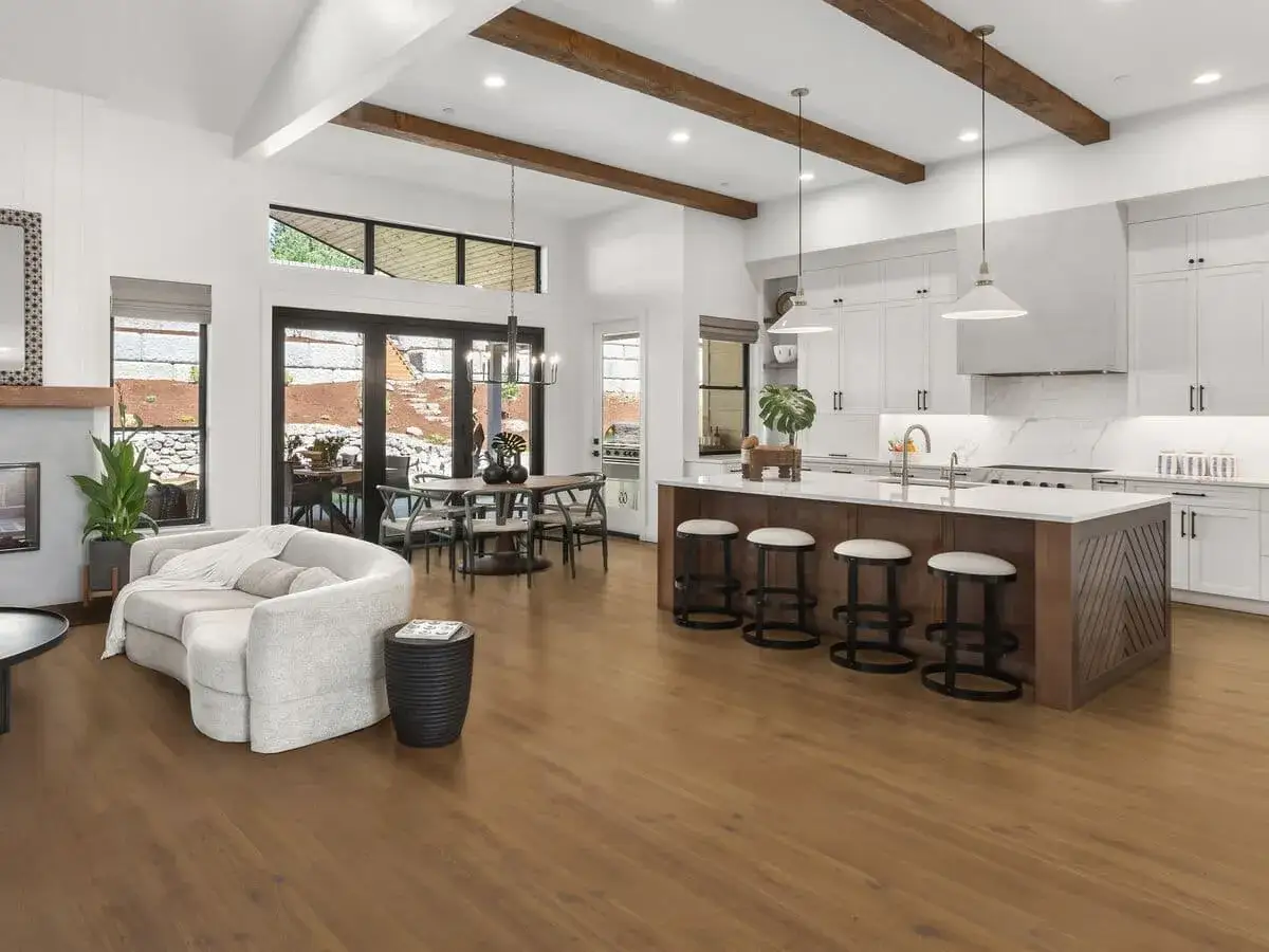 Amplio salón comedor con cocina abierta, isla central con taburetes y un sofá curvo. El suelo laminado o parquet de madera cálida une todos los espacios.