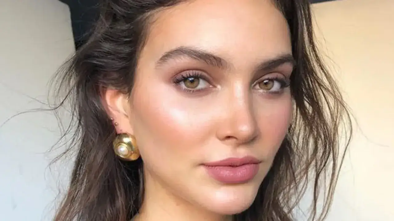 Maquillaje ojos marrones con sombras rosadas y labios nude. Destacan sus grandes pendientes dorados.