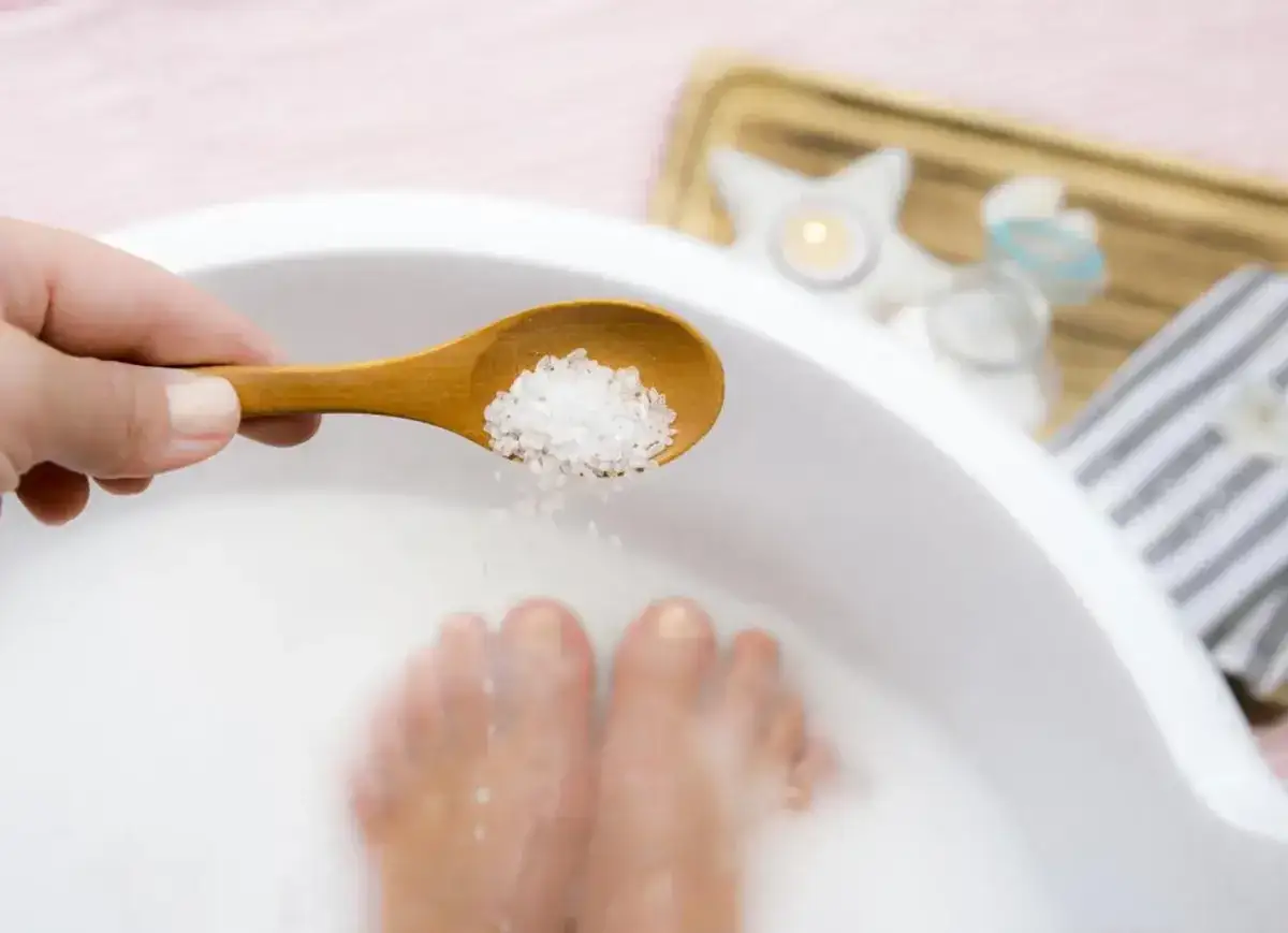 Une cuillère en bois verse du sel dans un bain de pieds. Une détente pour les pieds avec du bicarbonate et du vinaigre.