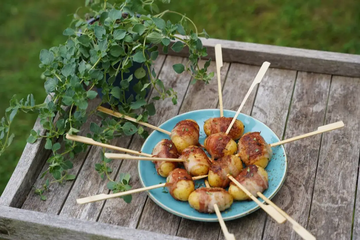 Köstliche Kartoffeln im Speckmantel auf Spießen, garniert mit Kräutern, auf einem blauen Teller auf einem Holztisch.
