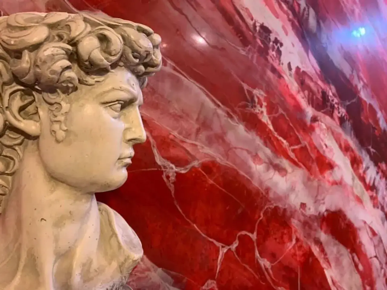 Busto in stile classico su sfondo rosso con venature bianche, un suggestivo stucco effetto marmo.