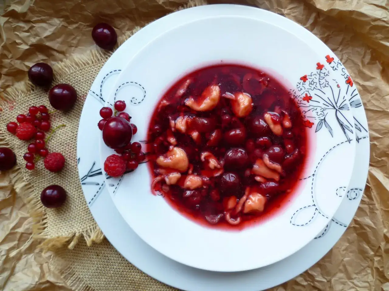Pyszna zupa owocowa z wiśniami i malinami, podana na talerzu z ozdobnym wzorem.
