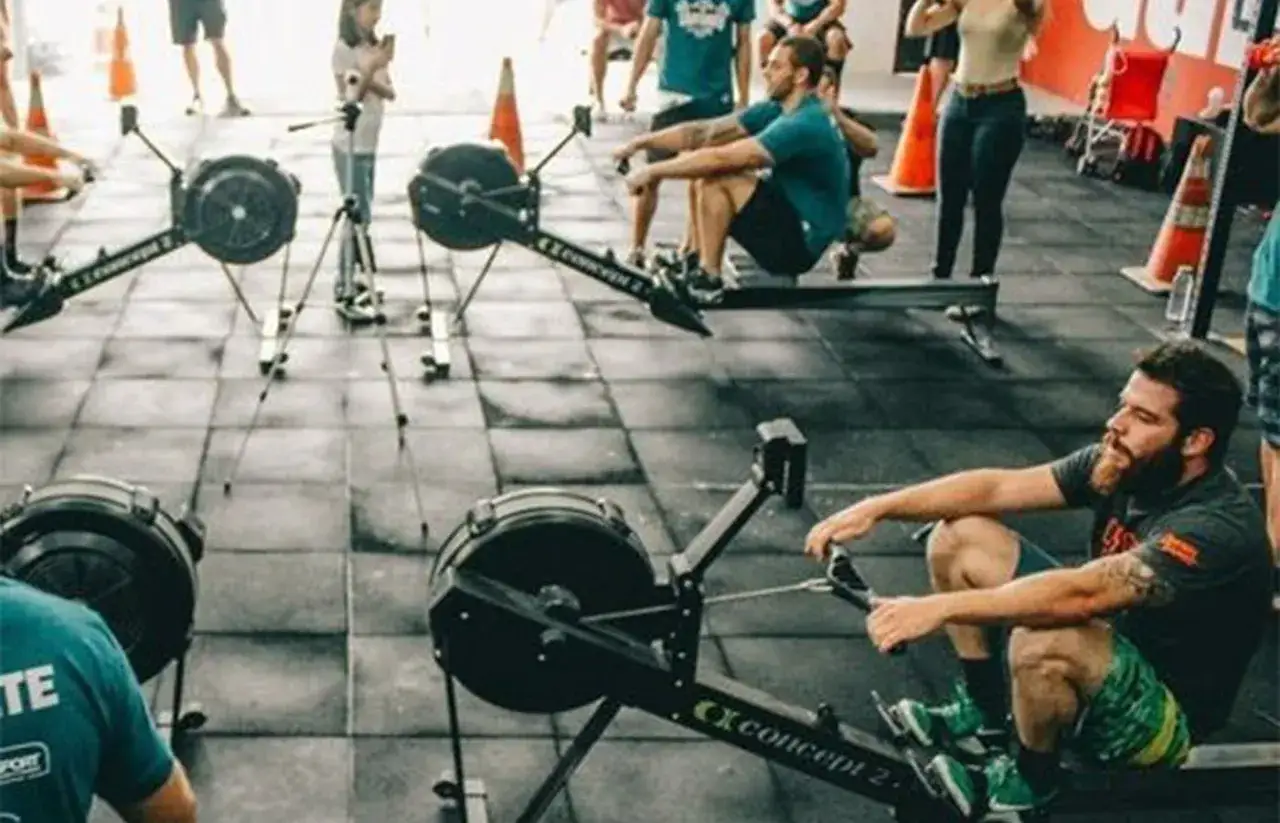 Ludzie ćwiczą na wioślarskich ergometrach. To właśnie crossfit co to za trening, który łączy różne dyscypliny.