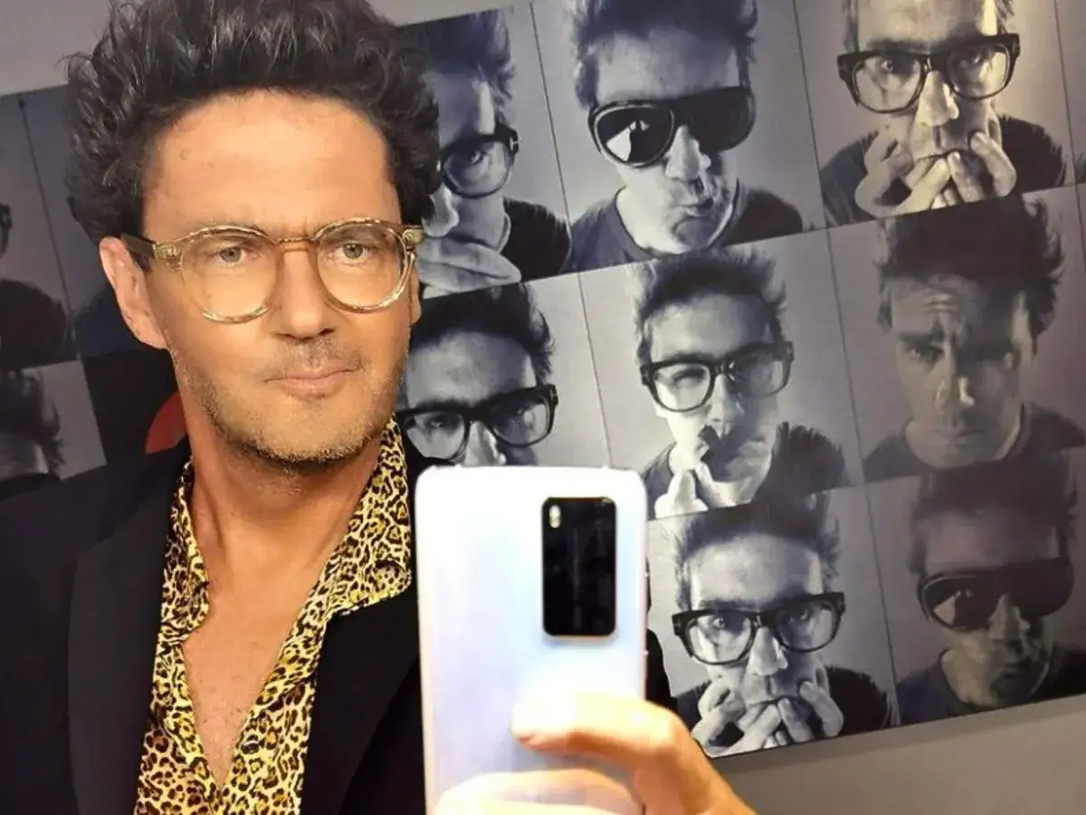 Znany dziennikarz w okularach, robi selfie na tle kolażu swoich zdjęć. To wyjaśnia, dlaczego znany dziennikarz nigdy nie pokazuje się publicznie bez okularów.