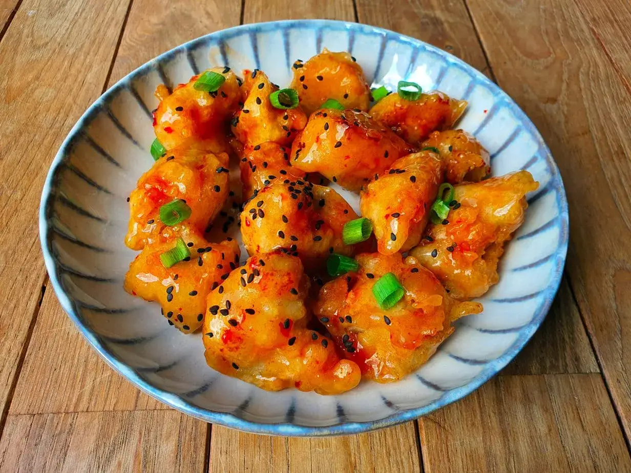 Krispig sweet chili kyckling med sesamfrön och salladslök på en blårandig tallrik.