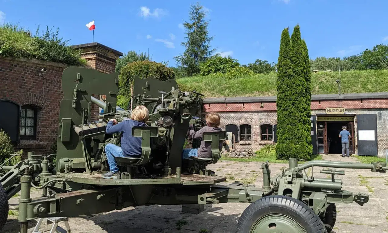 Dzieci bawią się przy działku na terenie fortu zachodniego. W tle budynek muzeum.