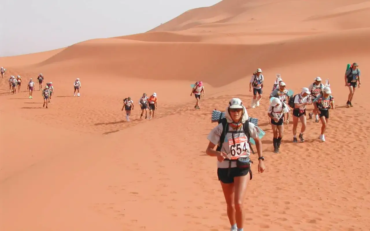 Teilnehmer des Marathon des Sables k&auml;mpfen sich durch die W&uuml;ste. Eine L&auml;uferin mit Startnummer 654 im Vordergrund.