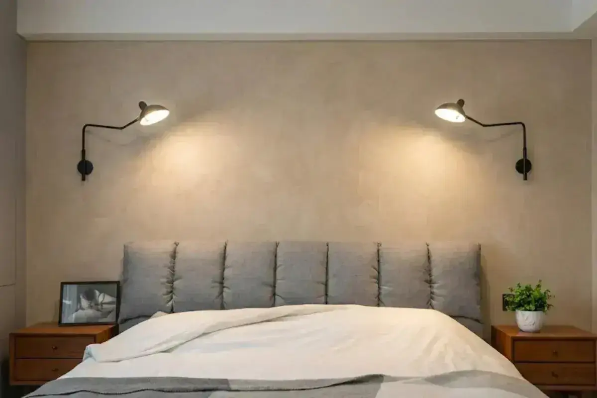 Appliques murales noires, réglables en hauteur, éclairent un lit confortable avec une tête de lit capitonnée.