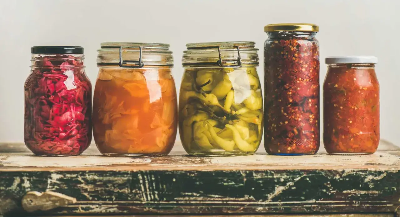 Fünf Gläser mit fermentierten, probiotischen Lebensmitteln: Rotkohl, Sauerkraut, eingelegte grüne Chilis, scharfe Paste und Tomaten-Chutney.
