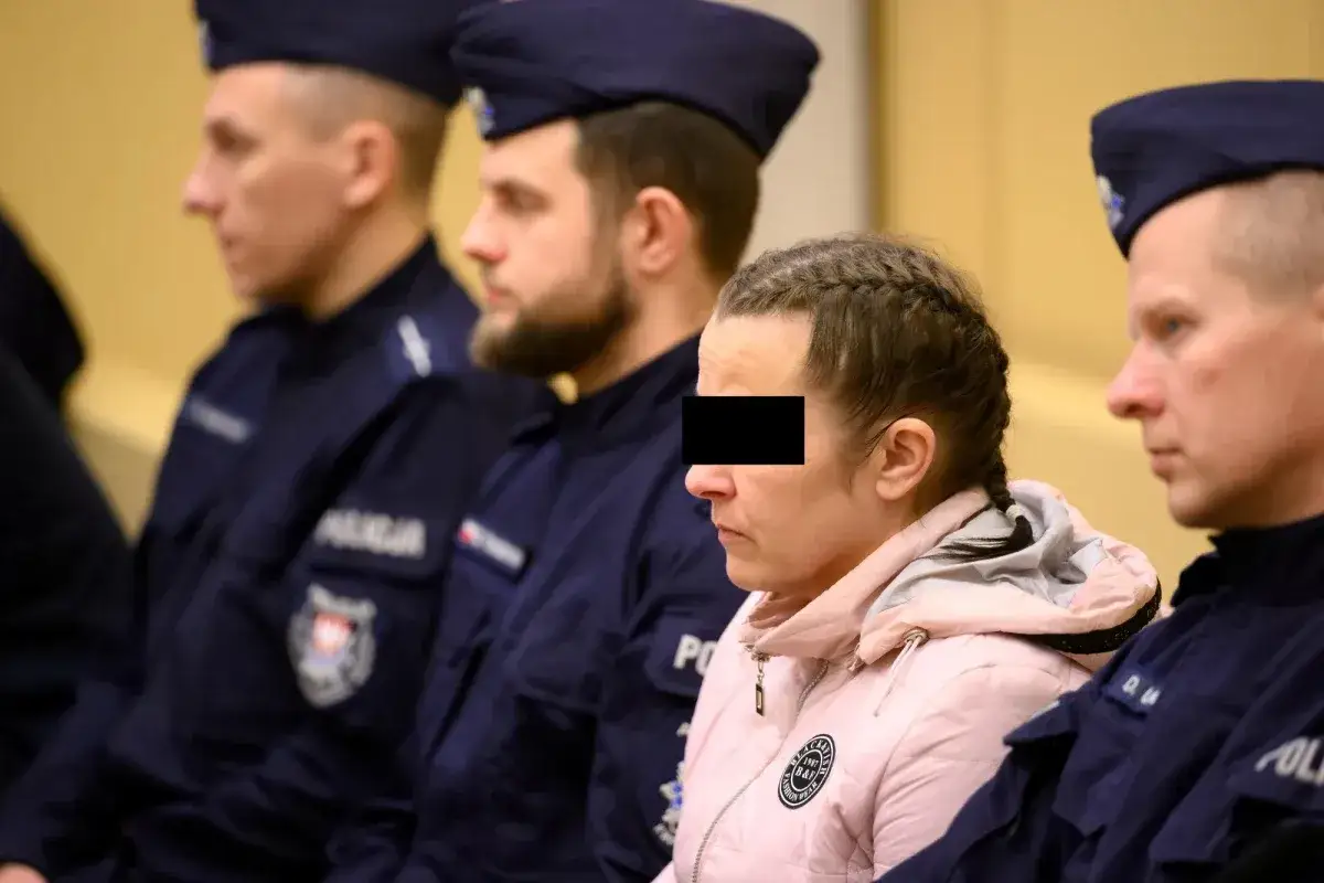 Kobieta z zakrytą twarzą siedzi w otoczeniu policjant&oacute;w, oczekując na wyrok.
