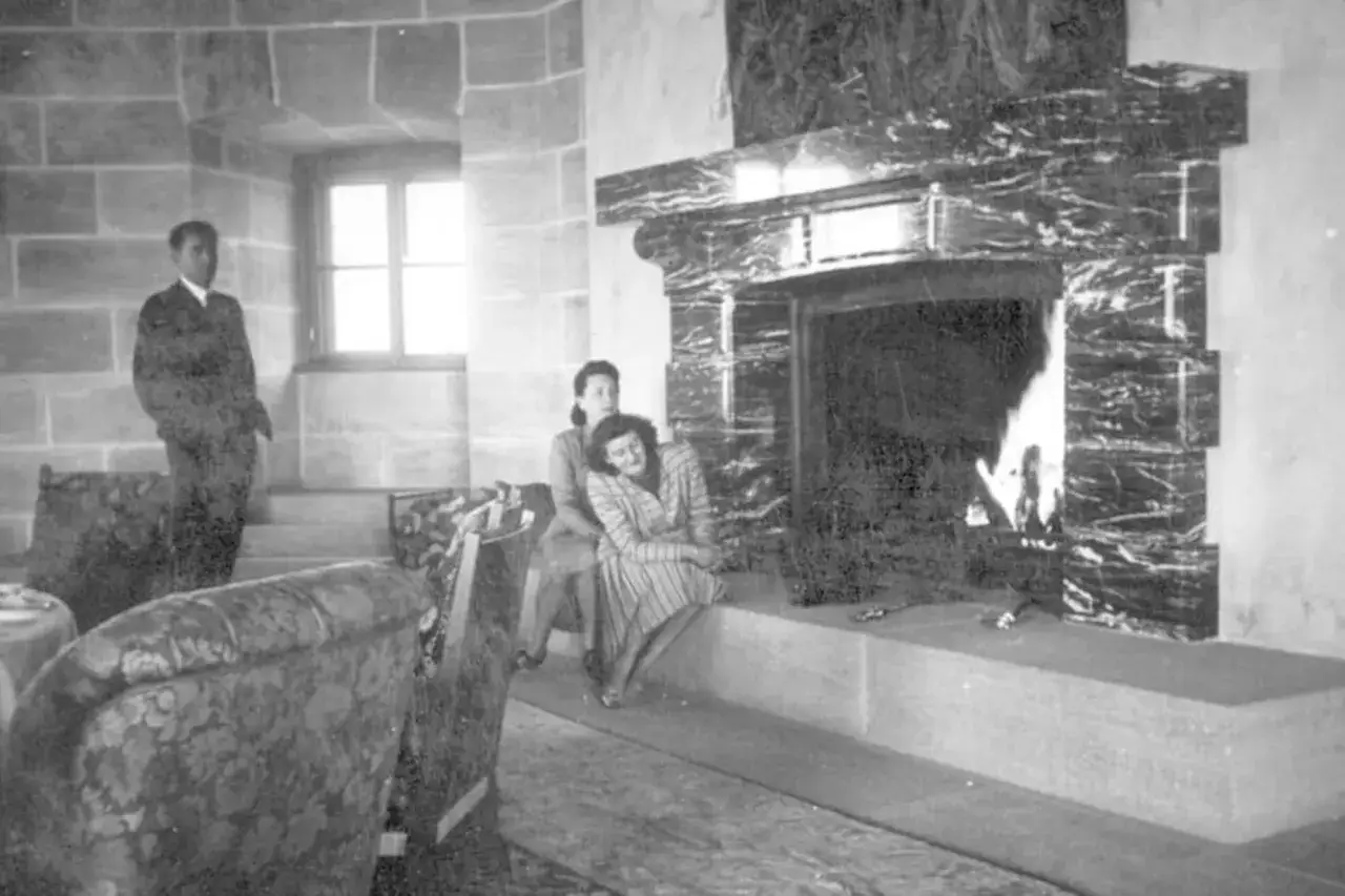 Zwei Frauen entspannen sich am Kamin im Kehlsteinhaus 1944. Ein Mann steht im Hintergrund.