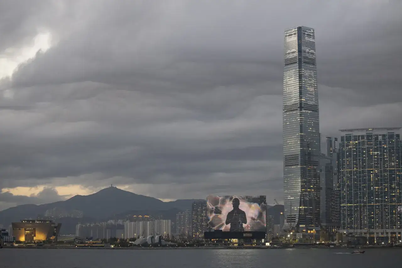 Hong Kong skyline at dusk, featuring a massive screen displaying a silhouette, hinting at the vibrant art scene of Art Basel Hong Kong 2026.