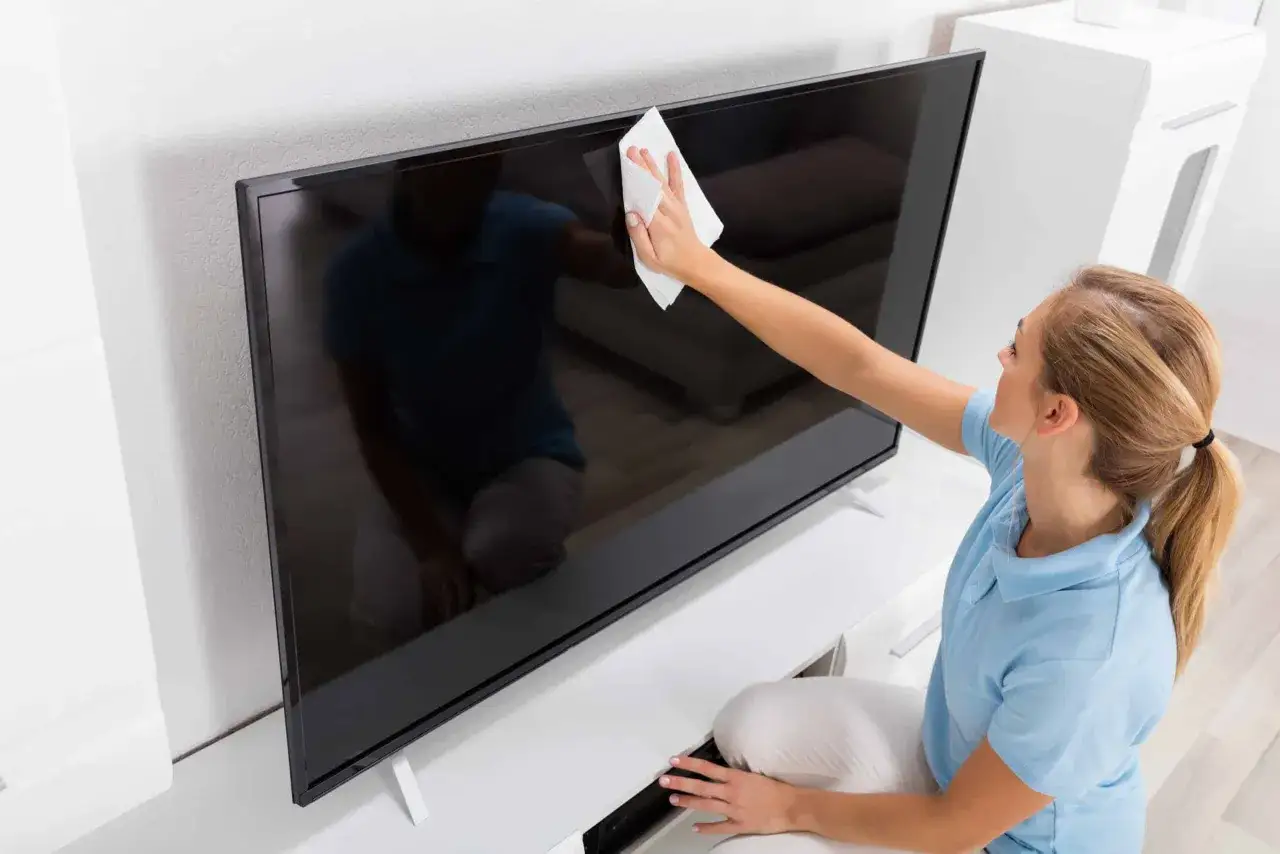 Kobieta delikatnie czyści ekran telewizora białą ściereczką, dbając o czystość sprzętu. Dowiedz się, czym umyć ekran telewizora, by był jak nowy.