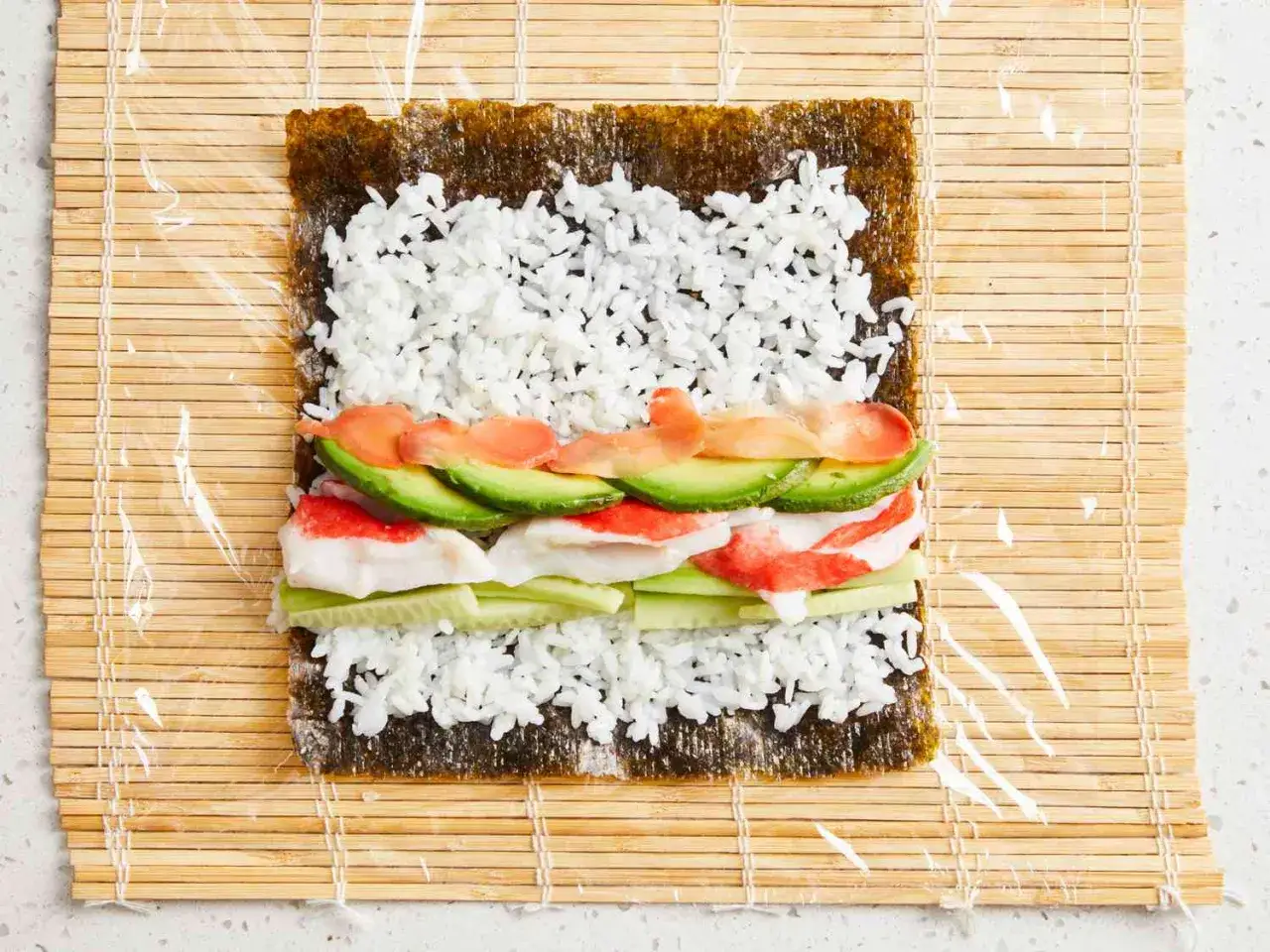 F&ouml;rberedelser f&ouml;r ett sushi recept: nori med ris, gurka, krabbstick, avokado och lax p&aring; en bambumatta.