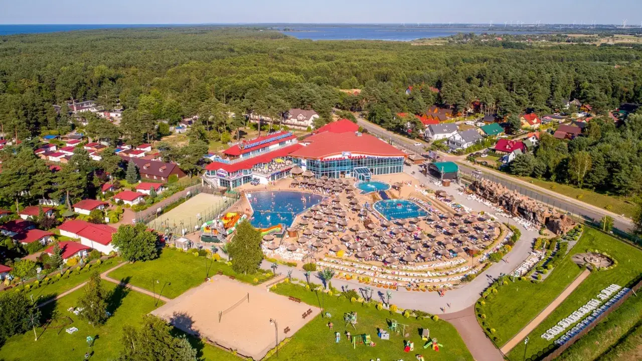 Ośrodek wypoczynkowy Panorama z basenami, zjeżdżalniami i leżakami, otoczony lasem i domkami.