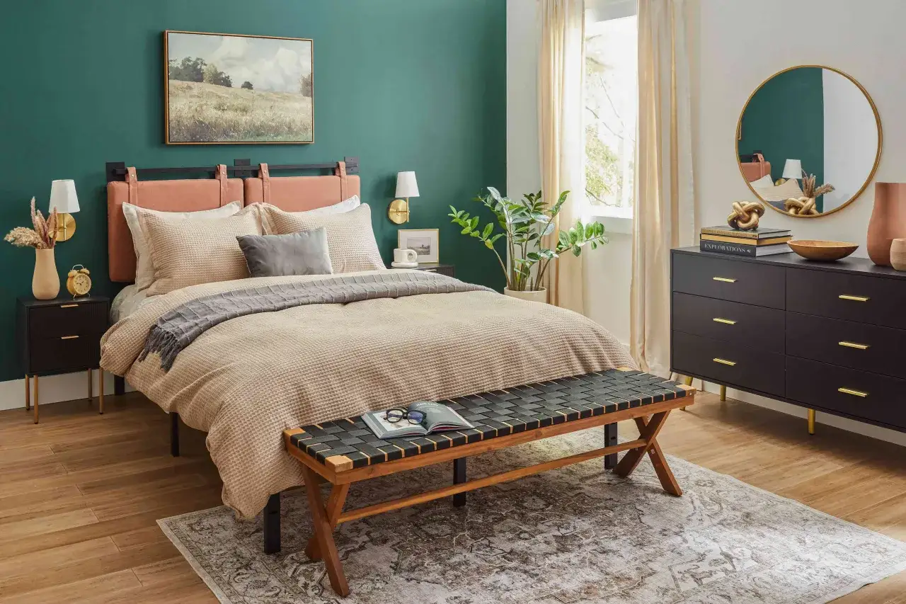 Une chambre aux murs vert &eacute;meraude et accents de bois. Un lit douillet, une commode sombre et un banc en bois compl&egrave;tent ce d&eacute;cor apaisant.