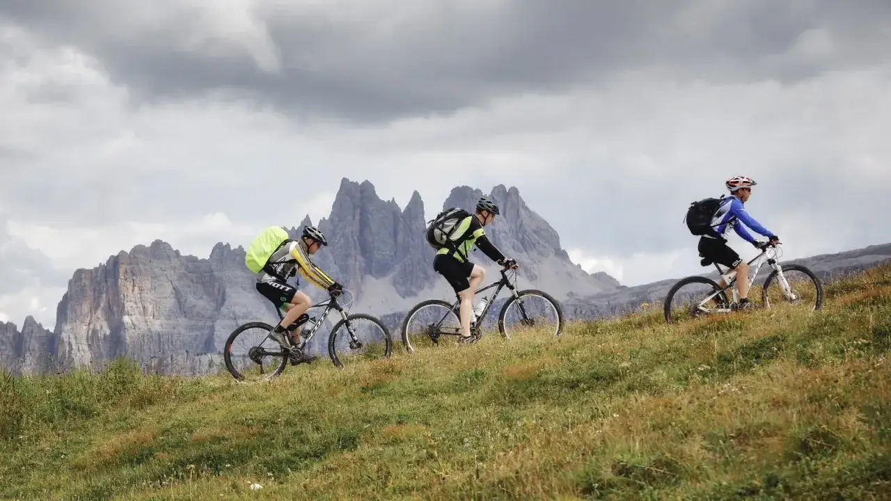 Three cyclists ride through a grassy mountain landscape, exploring some of the best cycling routes in Europe.