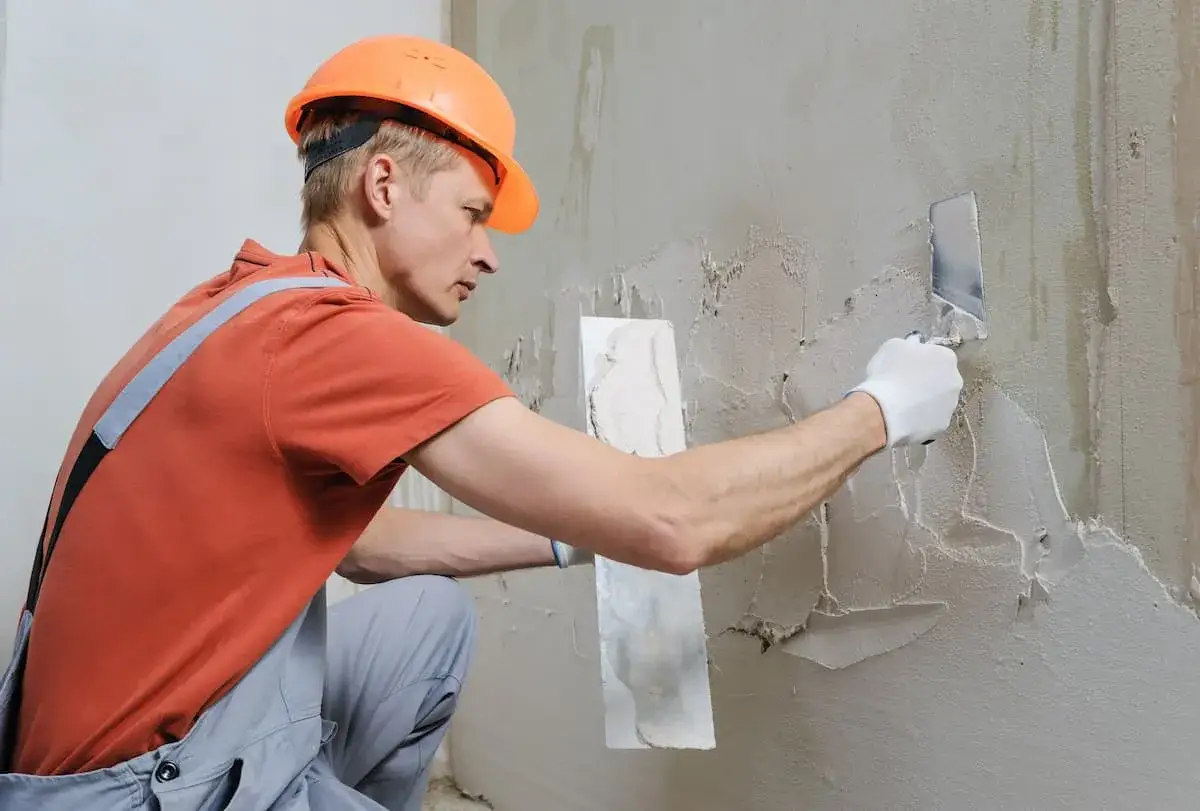 Bauarbeiter mit Schutzhelm verputzt eine Wand. Informieren Sie sich &uuml;ber die verputzen kosten f&uuml;r Ihr Projekt.