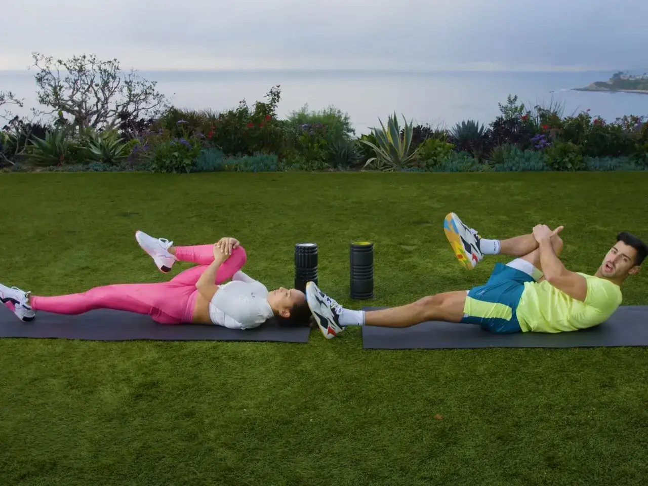 Couple faisant un exercice dos sur des tapis d'ext&eacute;rieur, avec vue sur l'oc&eacute;an.