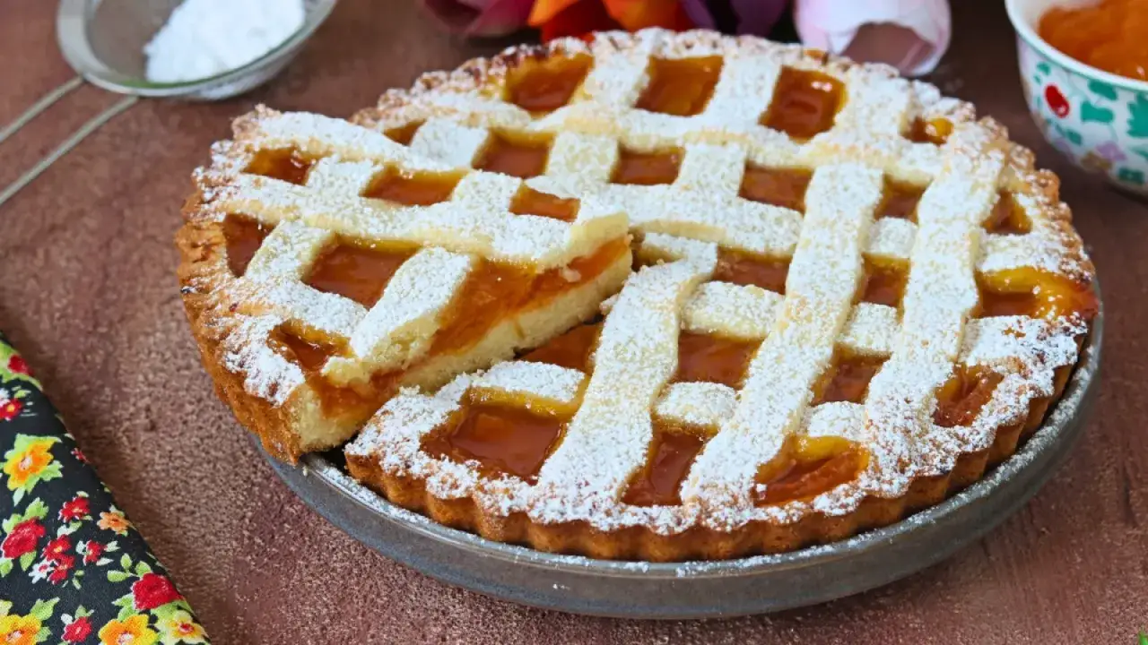 Crostata ricetta tradizionale con marmellata d'albicocche, cosparsa di zucchero a velo. Un dolce invitante e profumato.