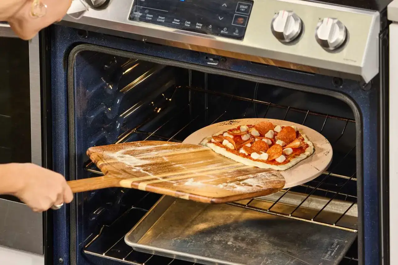Osoba wkłada pizzę do piekarnika, używając drewnianych łopatek do pizzy.