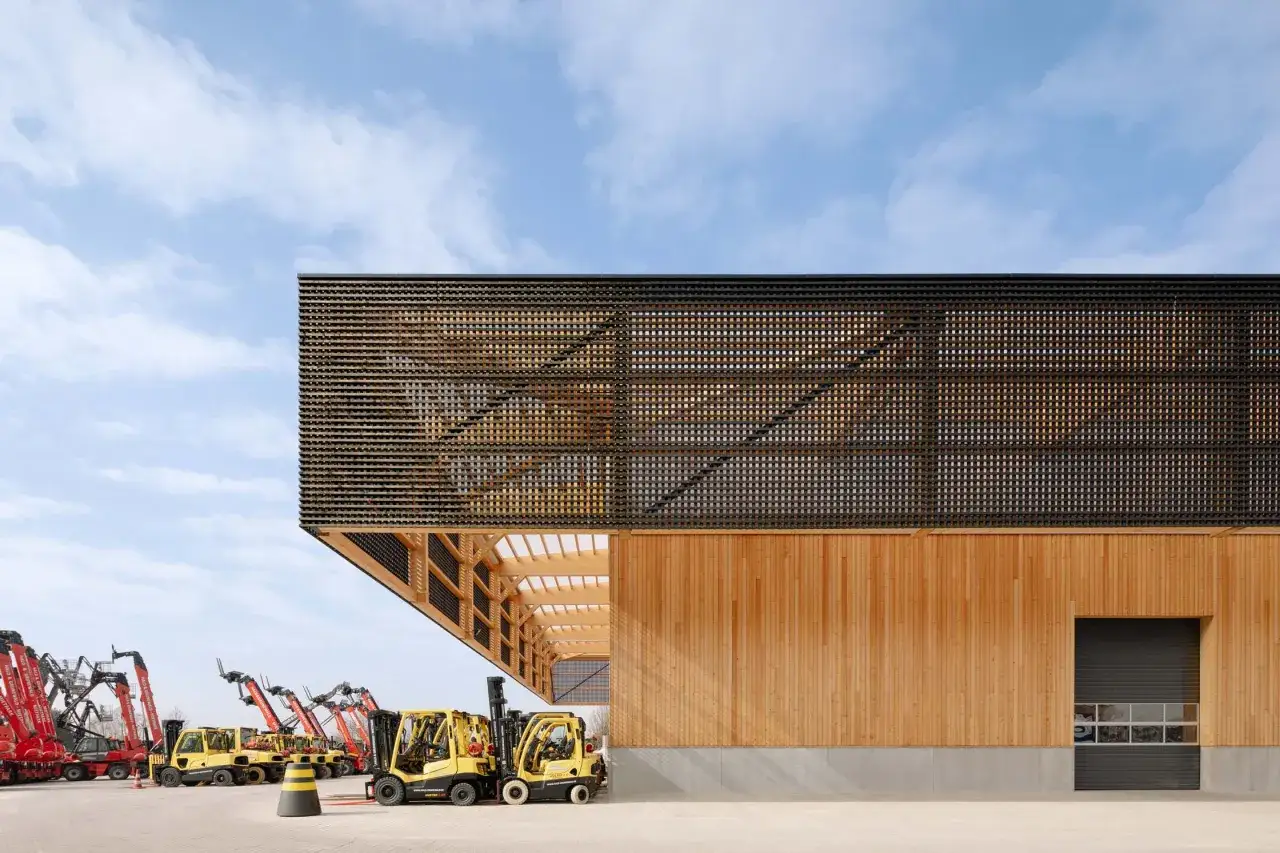 Moderne Halle mit Fassade aus hellem Holz und einem Gitter aus karbonisiertem Holz. Gabelstapler stehen davor.