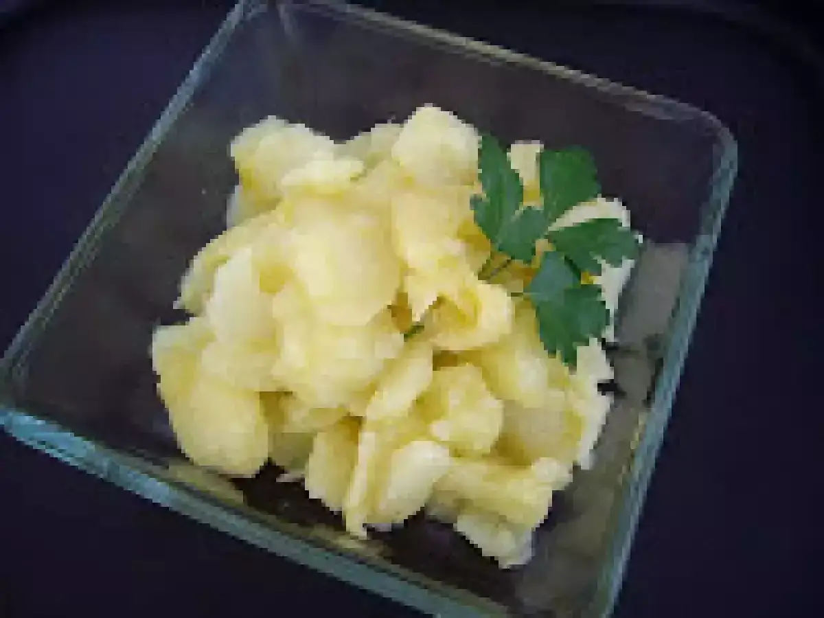 Patatas al montón, tiernas y doradas, servidas en un cuenco de cristal con una ramita de perejil.