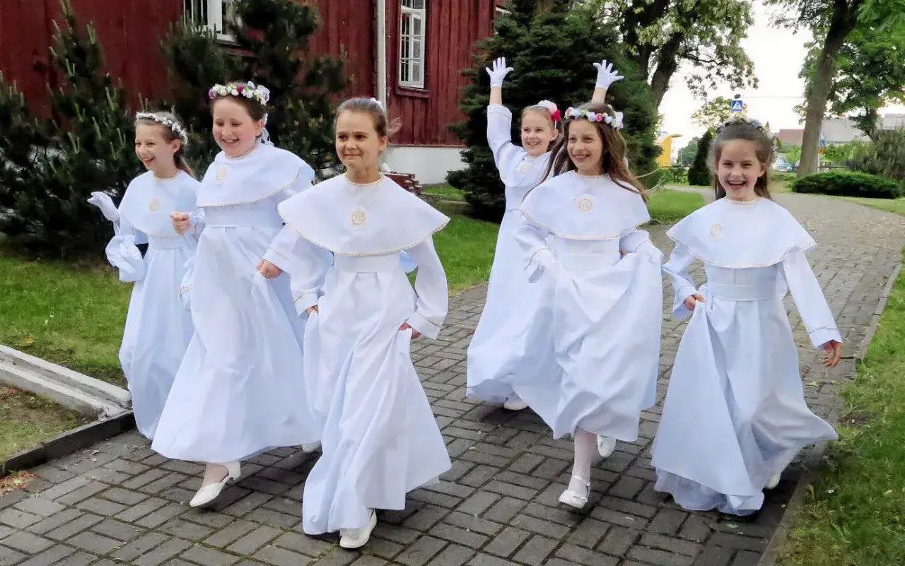 Radosny biały tydzień! Dzieci w białych strojach komunijnych biegną po chodniku, uśmiechnięte i pełne entuzjazmu.