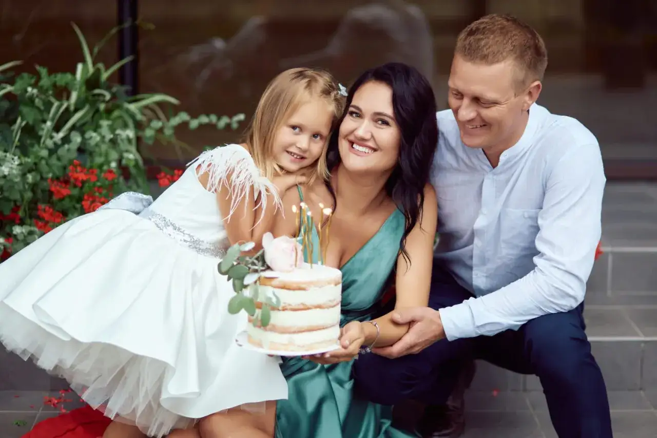 Famille souriante autour d'un g&acirc;teau d'anniversaire. La petite fille porte une robe blanche. La dur&eacute;e d'un bapt&ecirc;me civil est souvent courte, mais ce moment familial est pr&eacute;cieux.