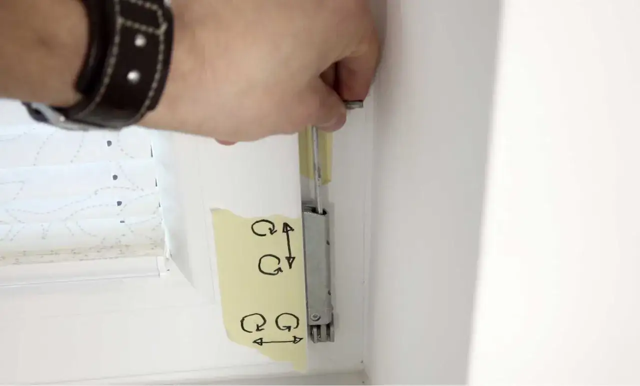Hand stellt mit Schraube das Fenster ein. Klebeband mit Pfeilen zeigt die Einstellrichtungen.